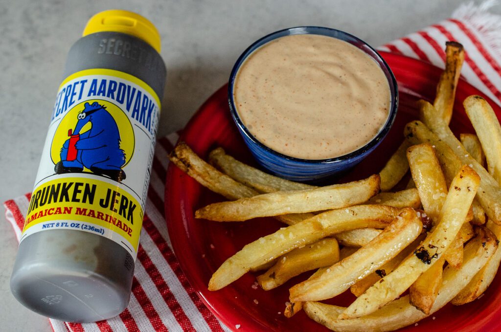a bowl of Drunken Fry Sauce plated with fries next to a bottle of Drunken Jerk Jamaican Marinade.