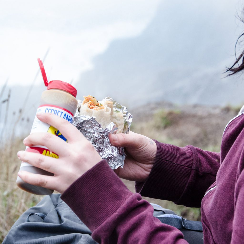 Person outdoors pouring Habanero Hot sauce onto a burrito