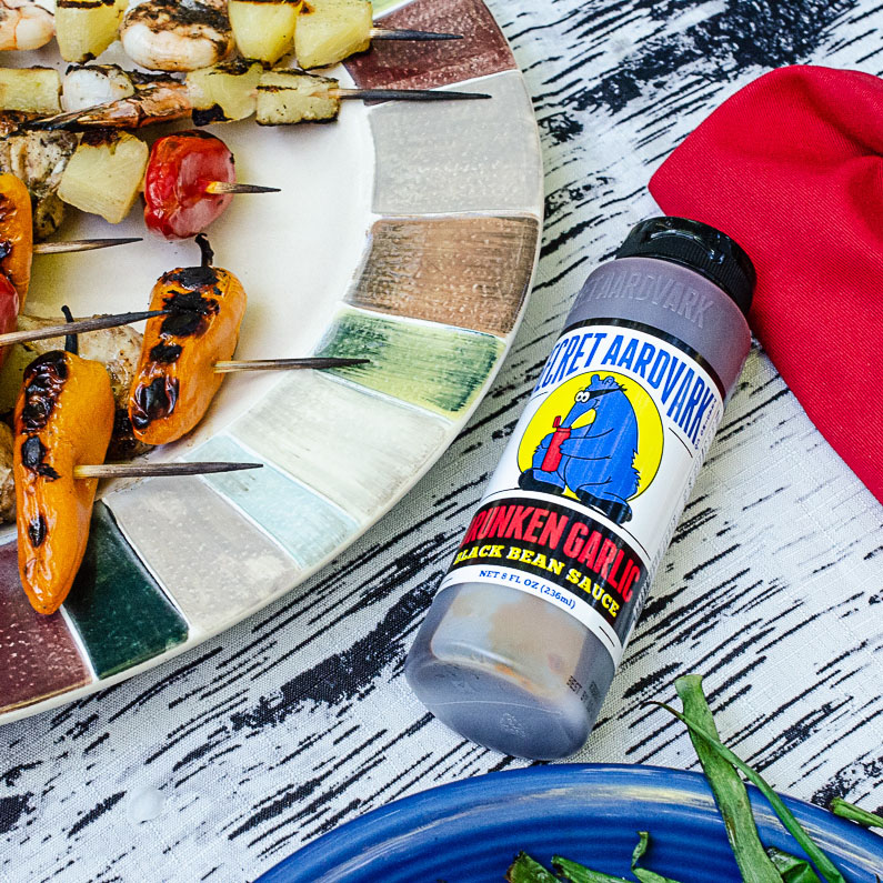 Secret Aardvark Drunken Garlic Black Bean Sauce bottle next to grilled shrimp skewers