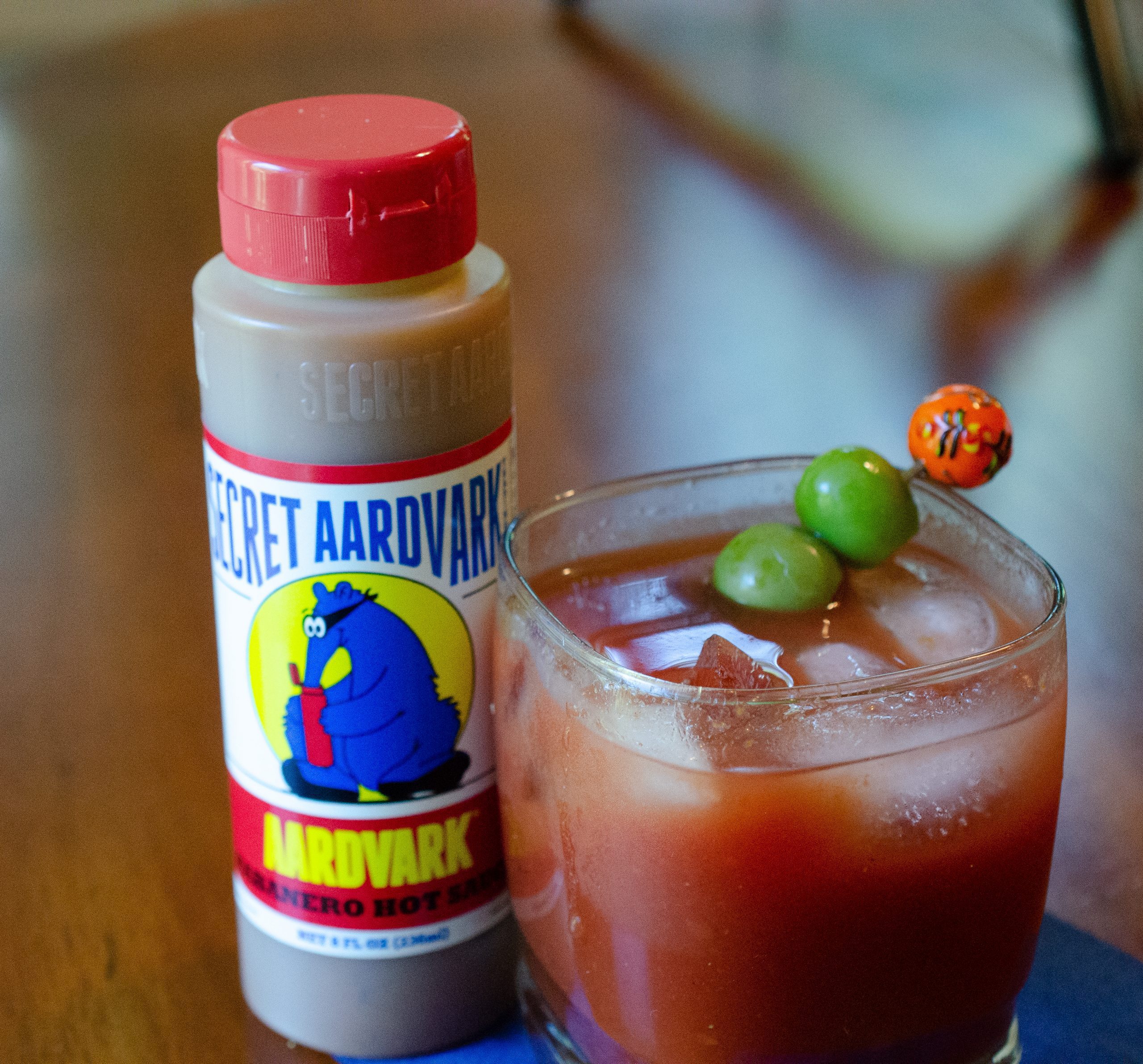A bloody mary and two olives as a garnish sitting next to a bottle of Aardvark Habanero hot sauce