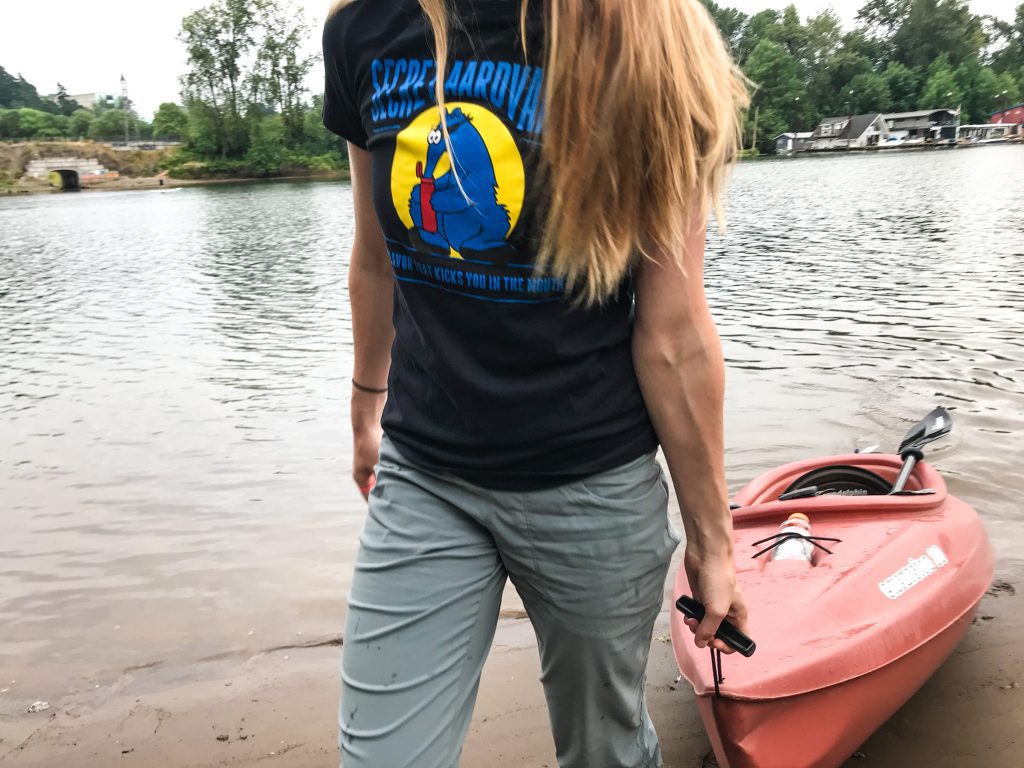 Woman pulling a kayak out of a river and wearing a secret aardvark t-shirt