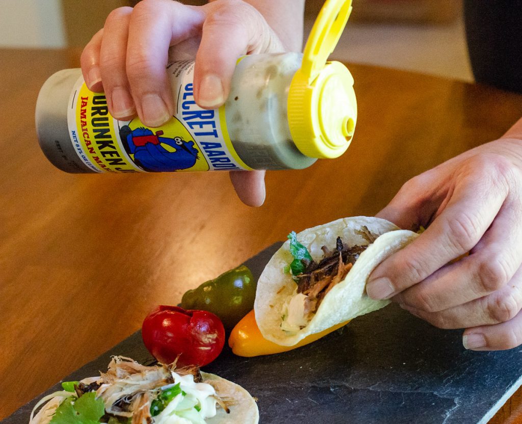 Person pouring a bottle of Jamaican Jerk Marinade onto a taco