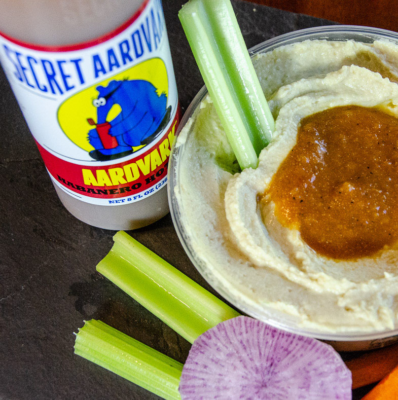 Secret Aardvark Habanero hot sauce next to hummus and celery sticks