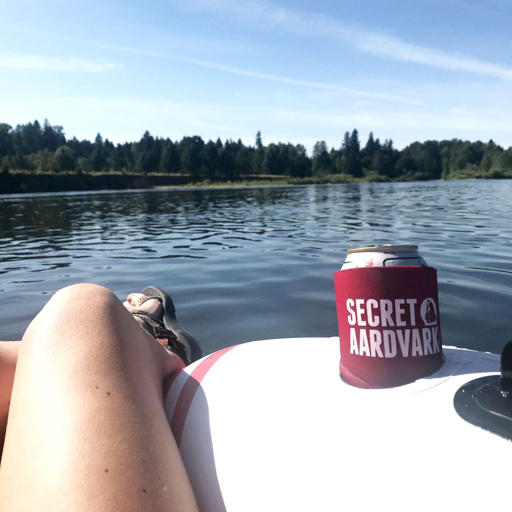 Sitting on an inner tube on a river with a drink in a Secret Aardvark koozie