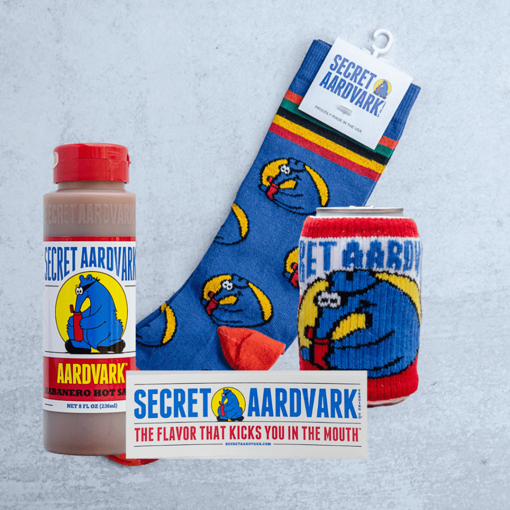 Super Fan Pack contents. 1 bottle of Aardvark Habanero Hot Sauce, 1 secret Aardvark sticker, 1 pair of crew socks, 1 Secret Aardvark Sweater Koozie