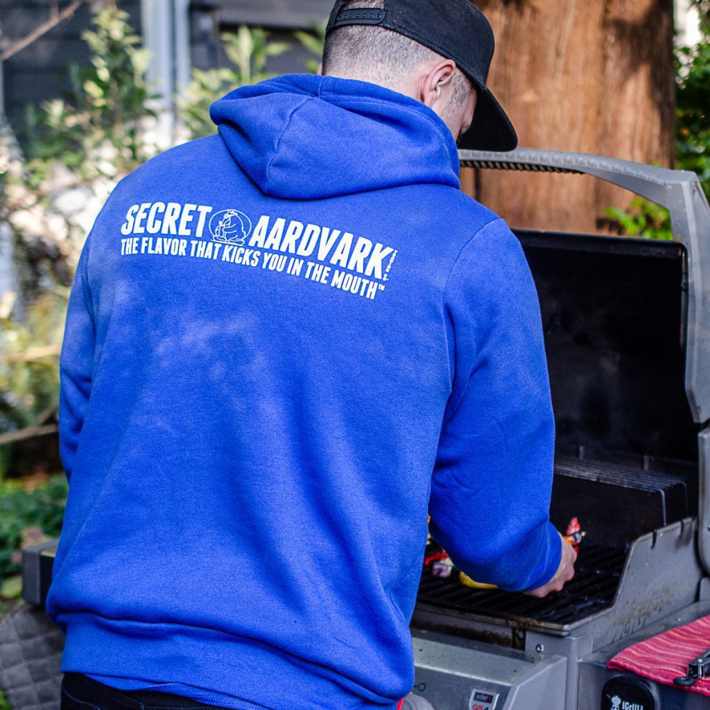 Man barbecuing food while wearing a blue secret aardvark hoodie