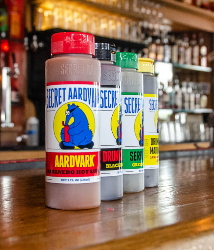 Bottles of Secret Aardvark sauces on a bar (Drunken Jerk, Aardvark Habanero, Drunken Garlic, and Serrabanero)