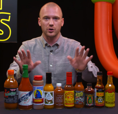 Person standing behind various hot sauces with hands up