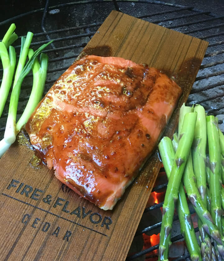 Salmon on cedar board next to asparagus and onions