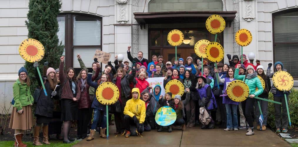 People in front of building holding protest signs and sunflower-shaped signs