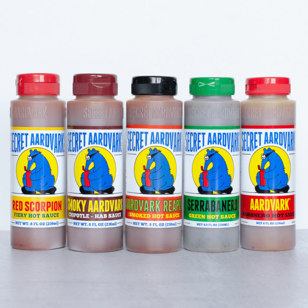 5 bottles of sauce lined up. Red Scorpion, Smoky Aardvark, Aardvark Smoked Reaper, Serrabanero Green Hot Sauce, Aardvark Habanero Hot Sauce.