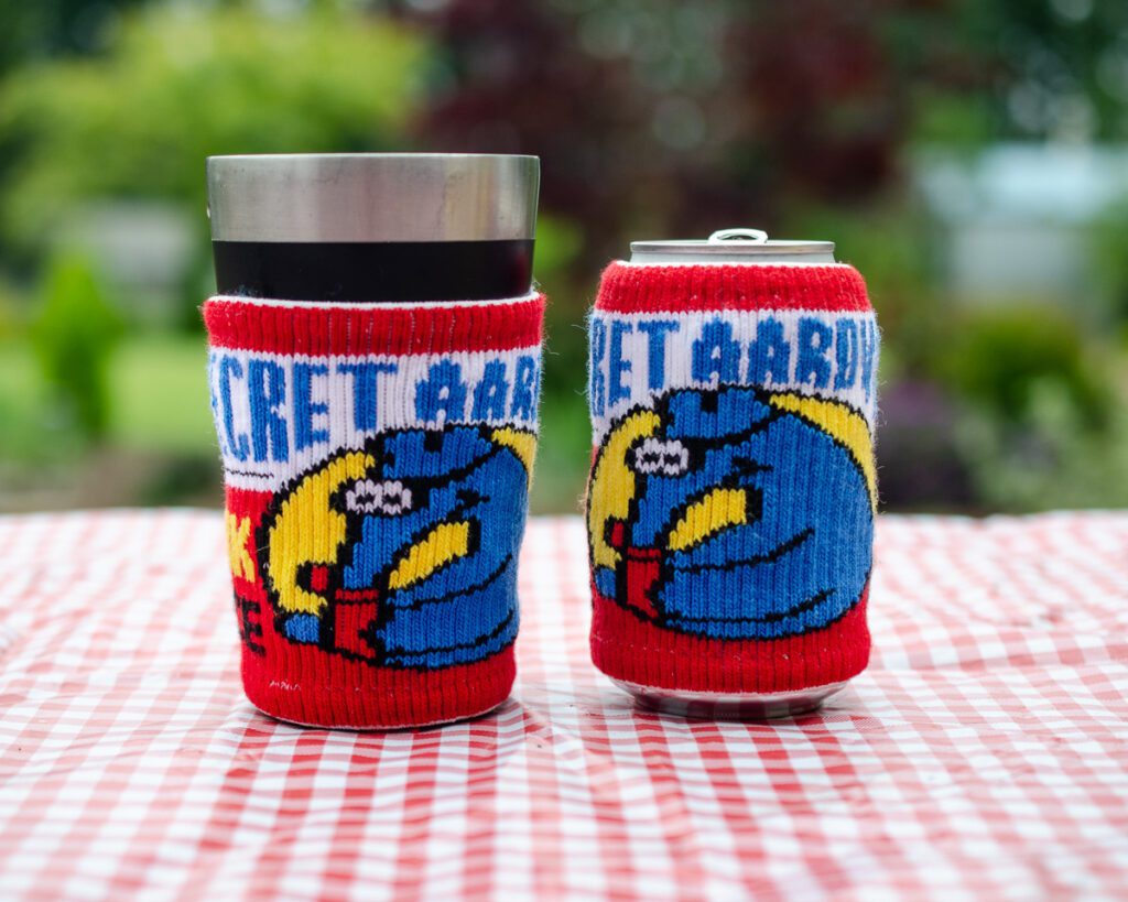 A cup and a can with Secret Aardvark sweater koozies