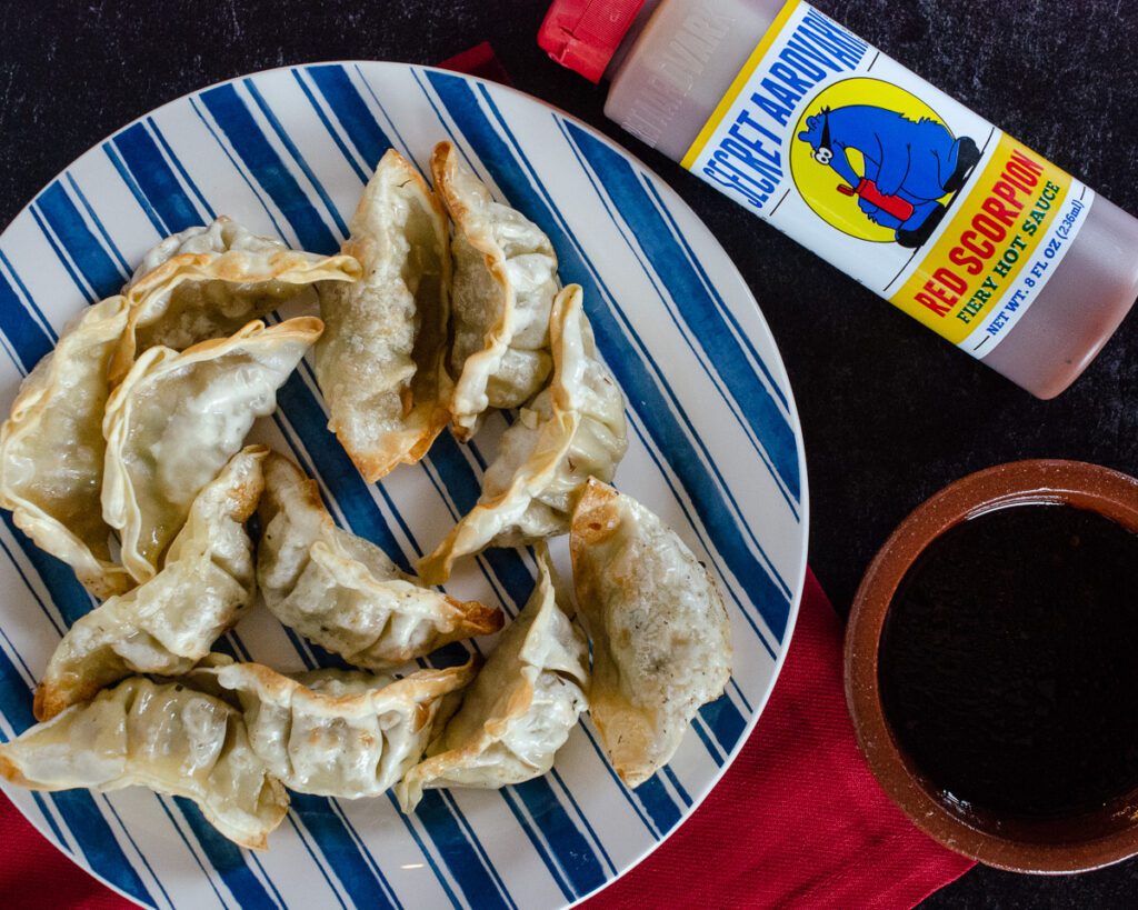 Plate of pot stickers next to a bottle of Red Scorpion Fiery Hot Sauce