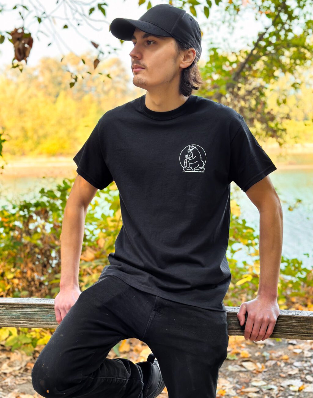 A man leaning on a fence wearing a black Secret Aardvark T-shirt.