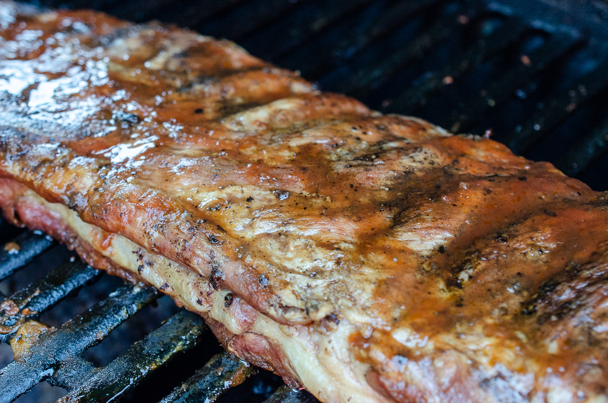 A rack of ribs cooking on a grill, slathered with Secret Aardvark Smoky Chipotle-Hab Sauce