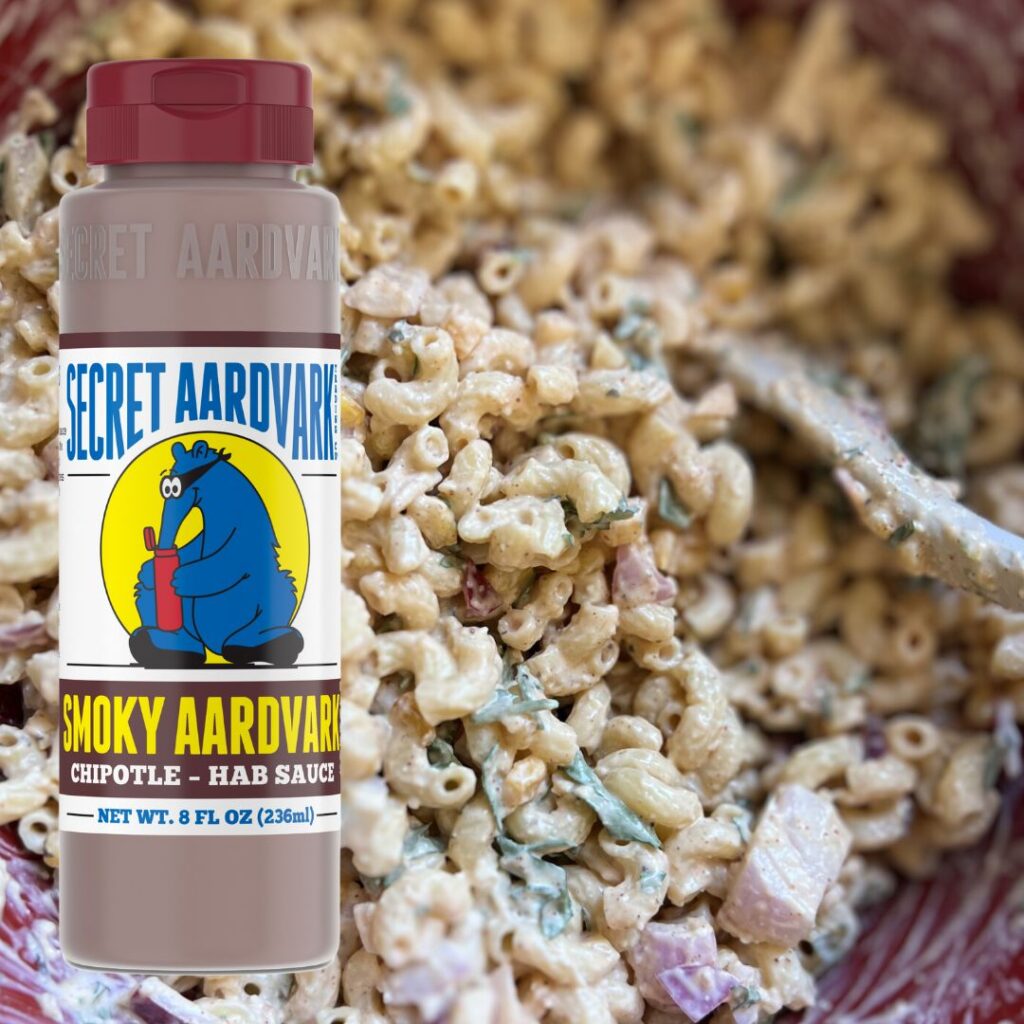A creamy bowl of elote pasta salad with a bottle of Aardvark Chipotle Sauce.