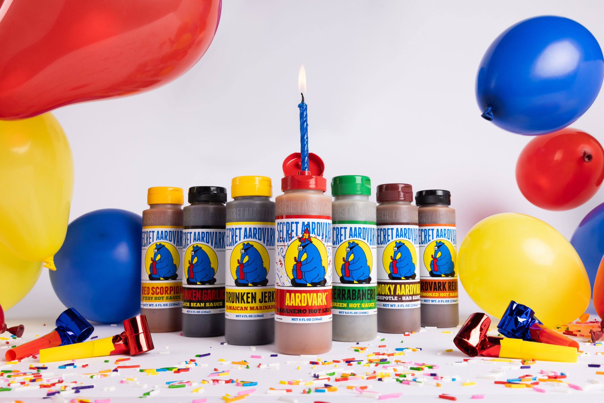 All 7 Aardvark sauce sand marinades on a table with a birthday candle, balloons, and confetti.