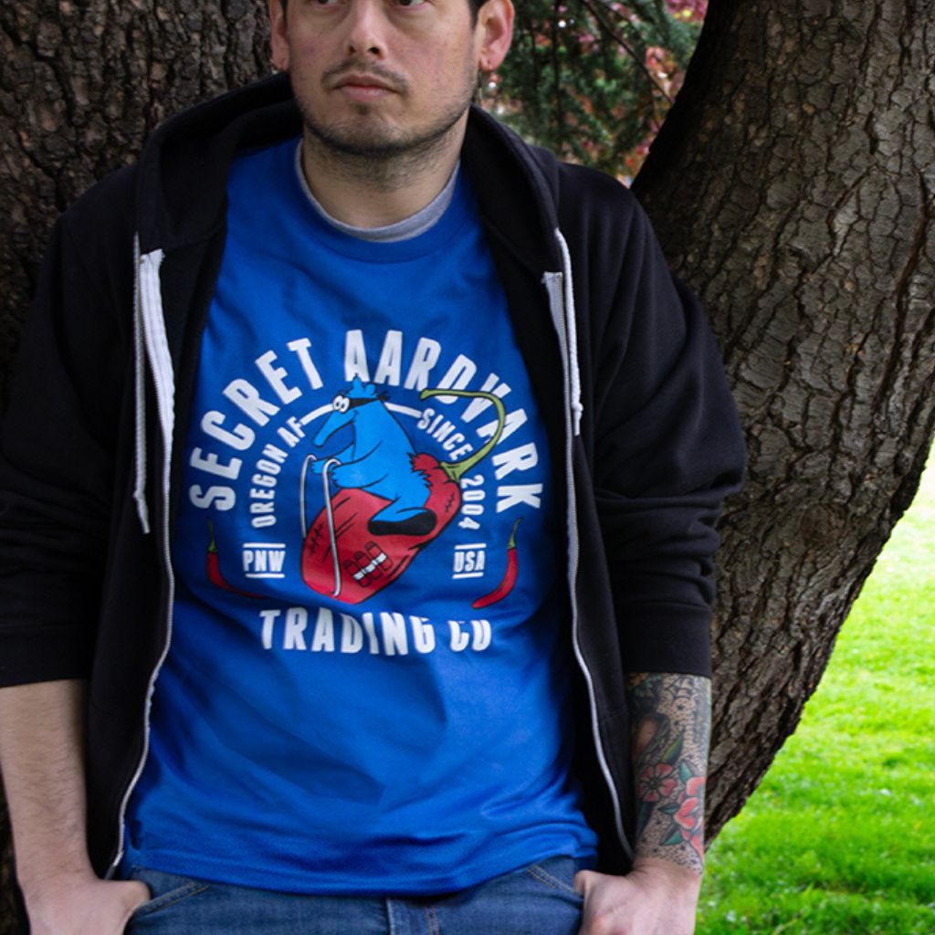 Man leaning against tree with blue Secret Aardvark t-shirt