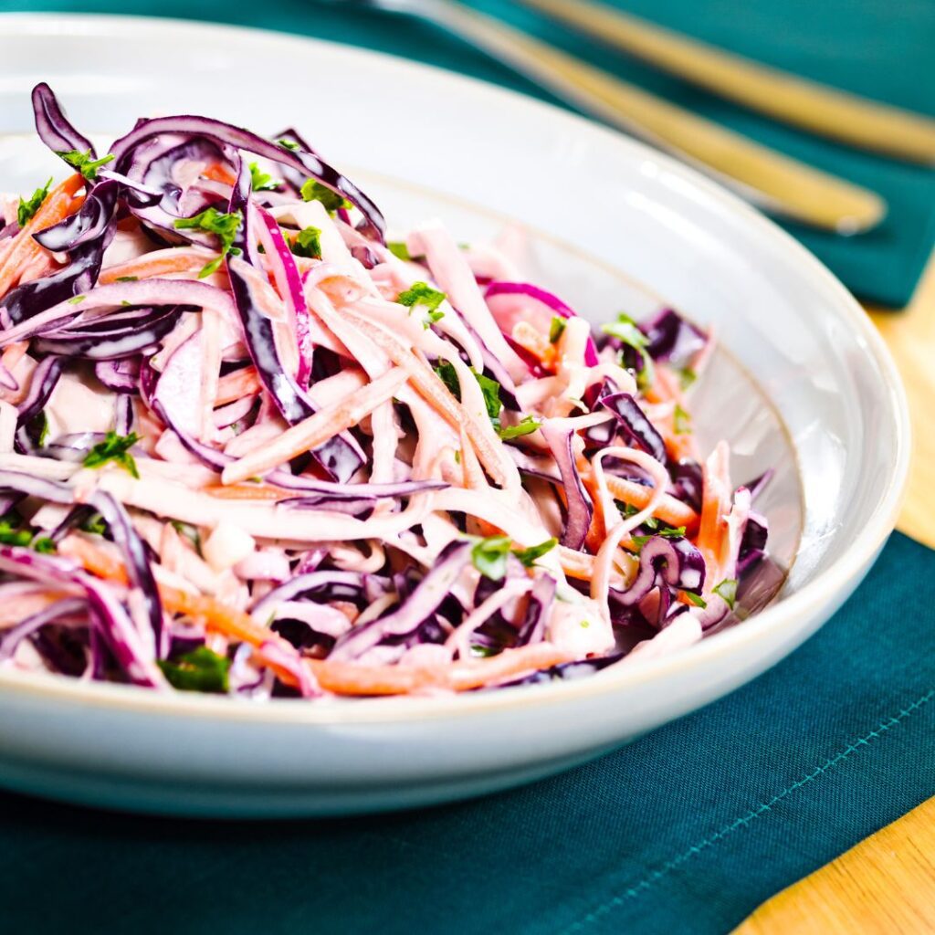 A beautiful bowl of coleslaw with red cabbage in a white bowl on a green placemat.