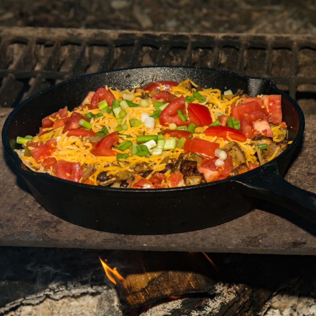 A cast iron skillet full of nachos being warmed over a fire. 