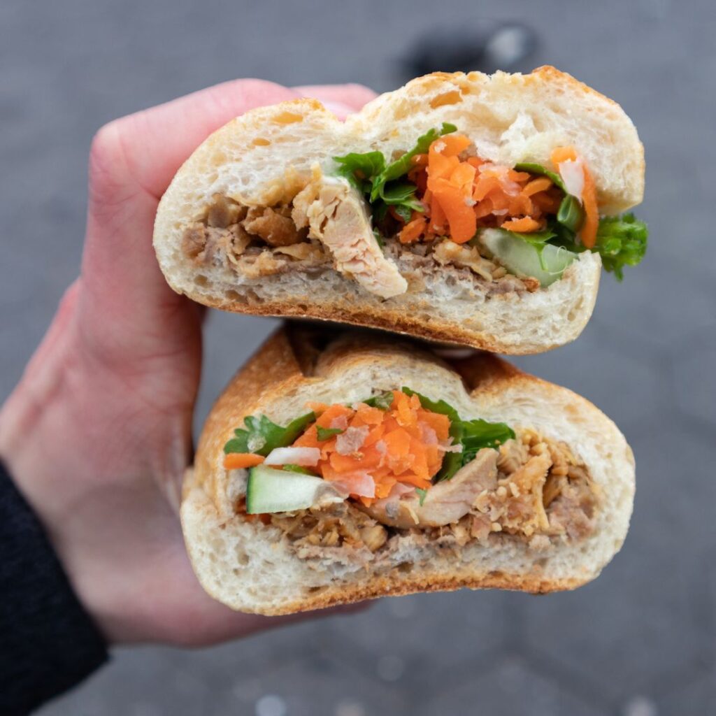 A beautiful Bahn Mi sandwich cut in half and held with a hand to show its fillings.