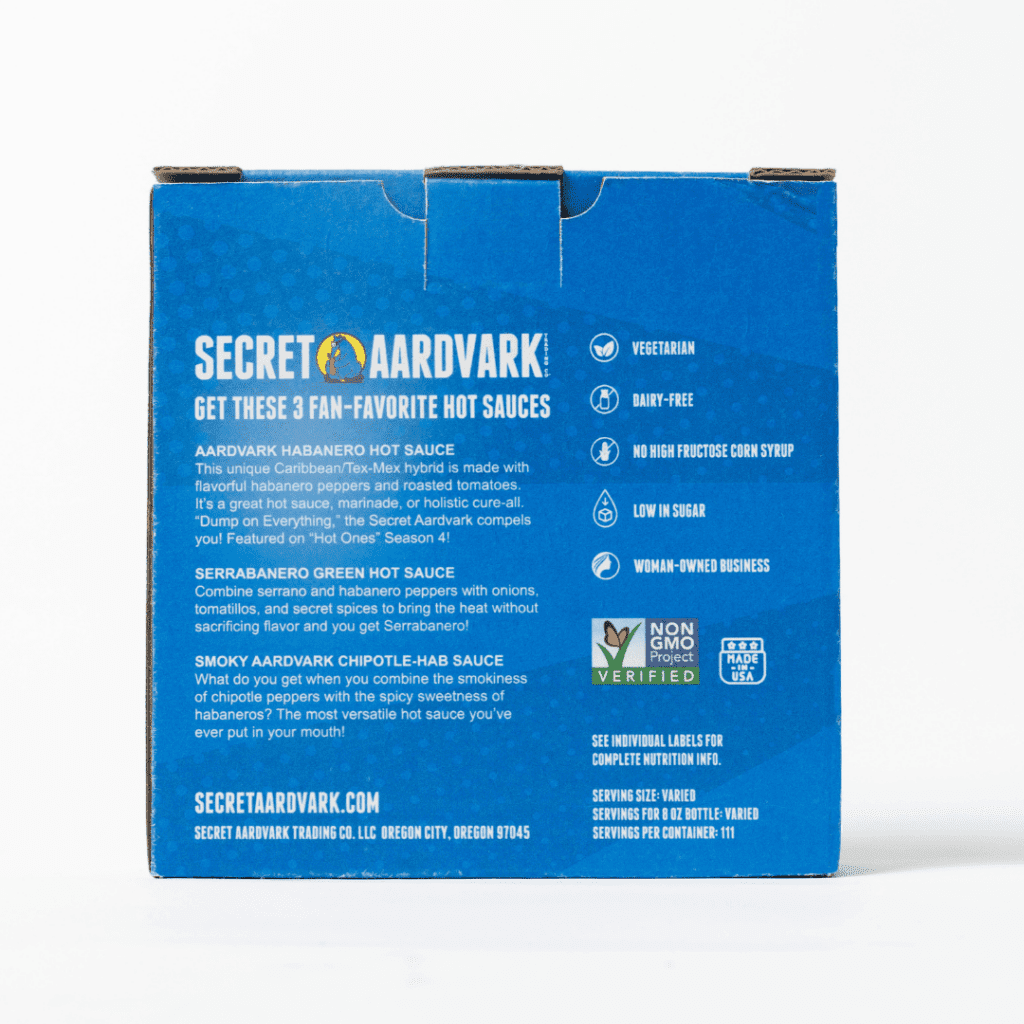 Backside of Blue 3pk Secret Aardvark Hot Sauce gift box. Box has description of the three hot sauces in box: Aardvark Habanero Hot Sauce, Serrabanero Green Hot Sauce, and Smoky Aardvark Chipotle-Hab Sauce.